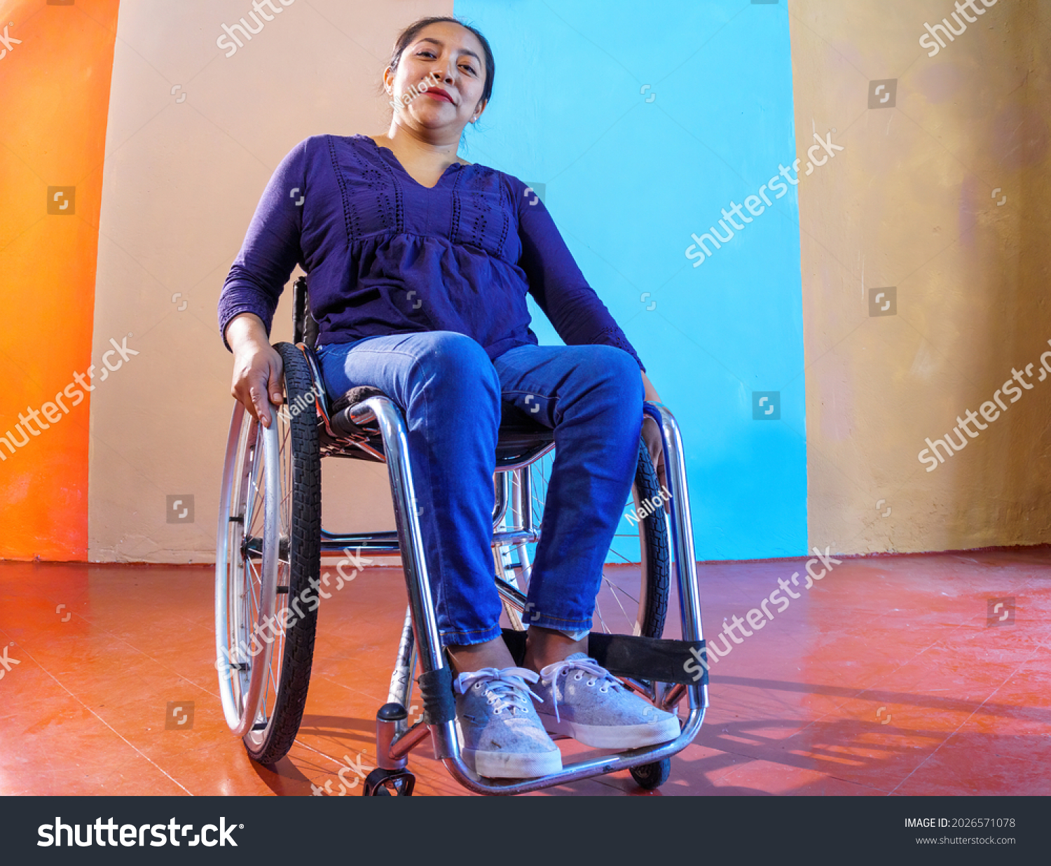 Middle-aged Hispanic woman with disabilities on a wheelchair against a colorful background #2026571078