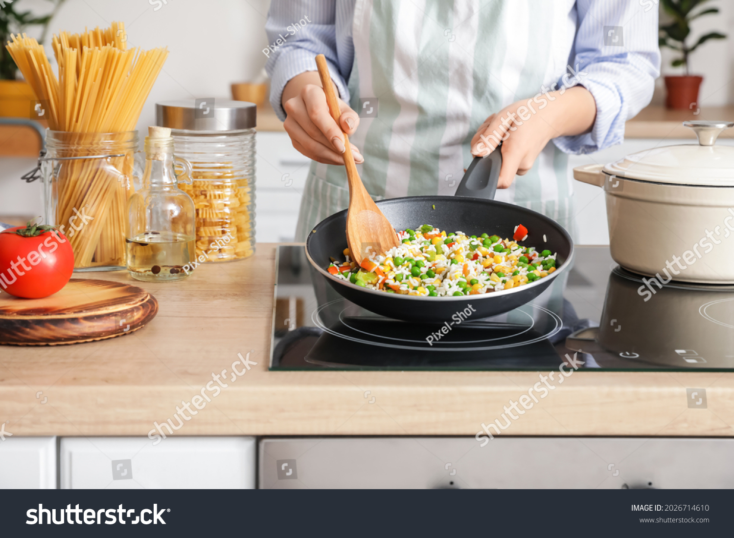 Woman cooking tasty rice with vegetables on stove in kitchen, closeup #2026714610