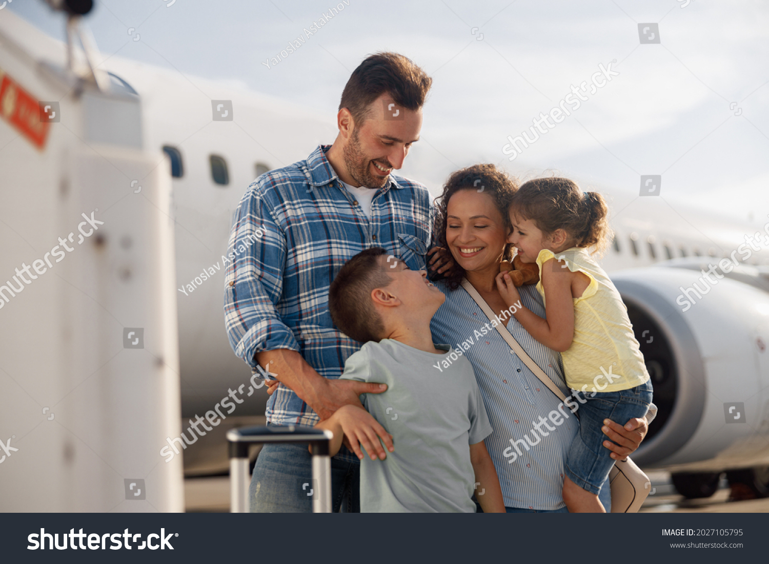 Family of four looking excited while going on a trip, standing in front of big airplane outdoors. People, traveling, vacation concept #2027105795