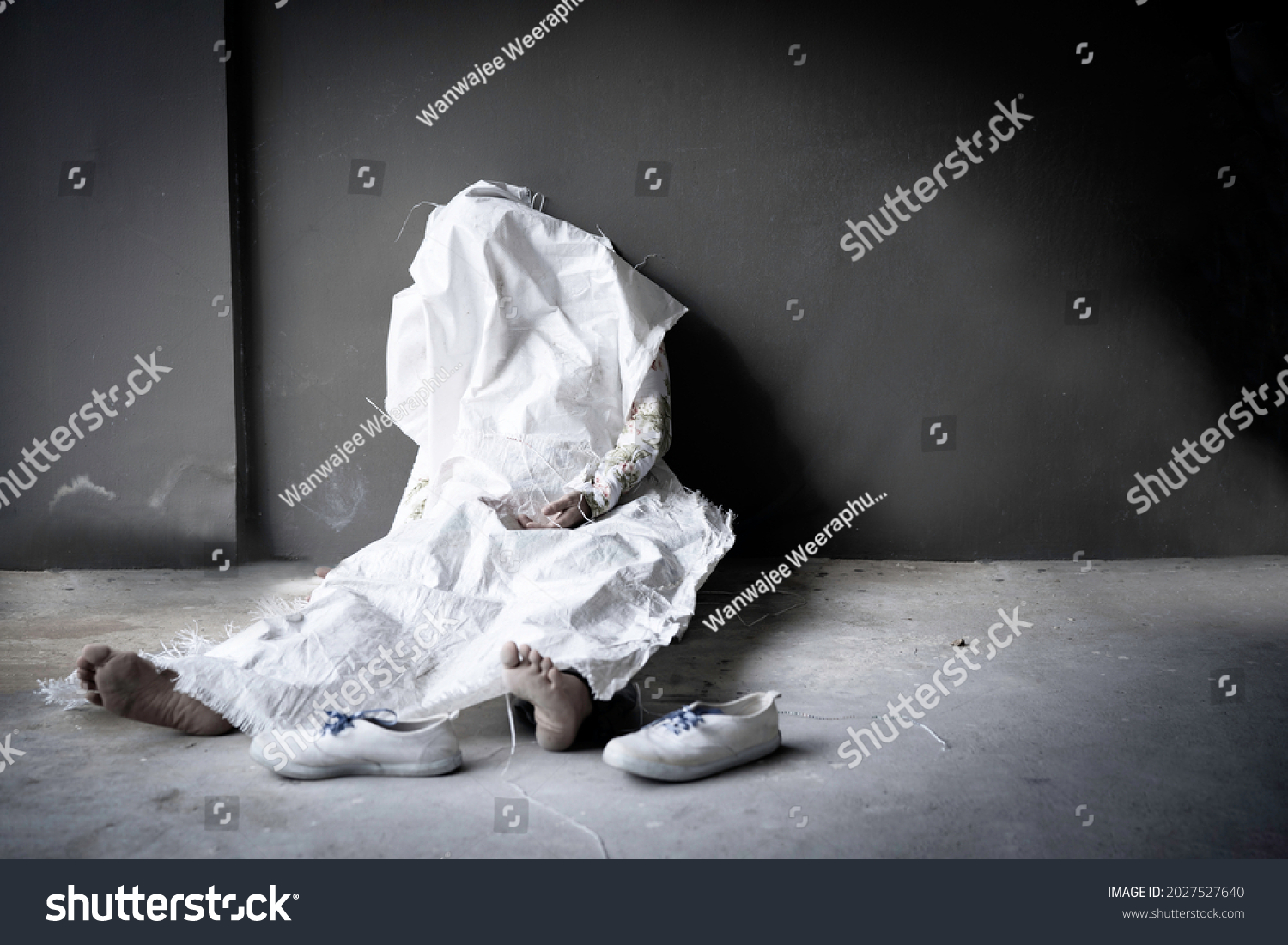 Dead person die in sitting position againt dark brown wall and concret floor with blurred shoes and bare foot was wrapped by white sack with copy space. #2027527640