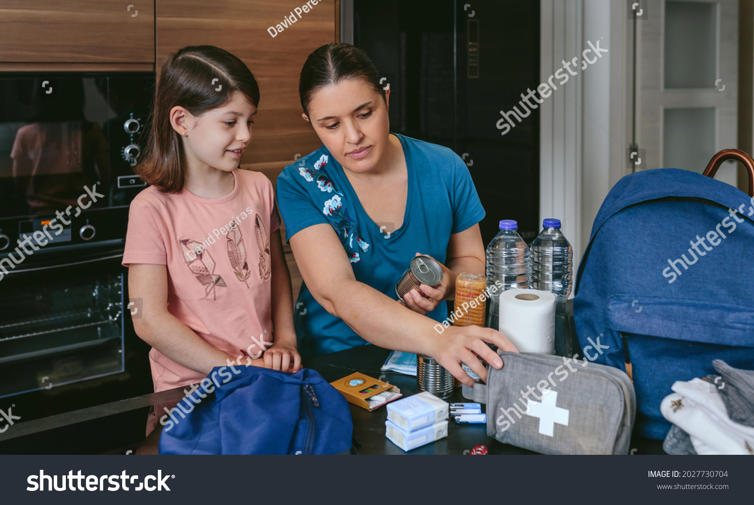 Mother preparing emergency backpack with her daughter in the kitchen #2027730704