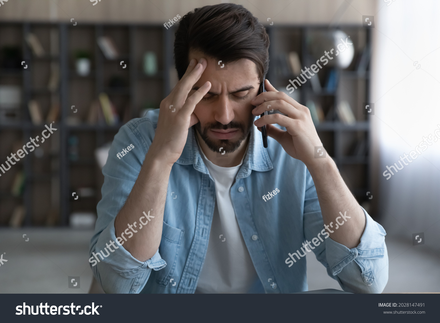 Stressed young man holding cellphone conversation, feeling displeased with bad negative news. Unhappy nervous male client dissatisfied with failure, listening debt notification, bankruptcy concept. #2028147491