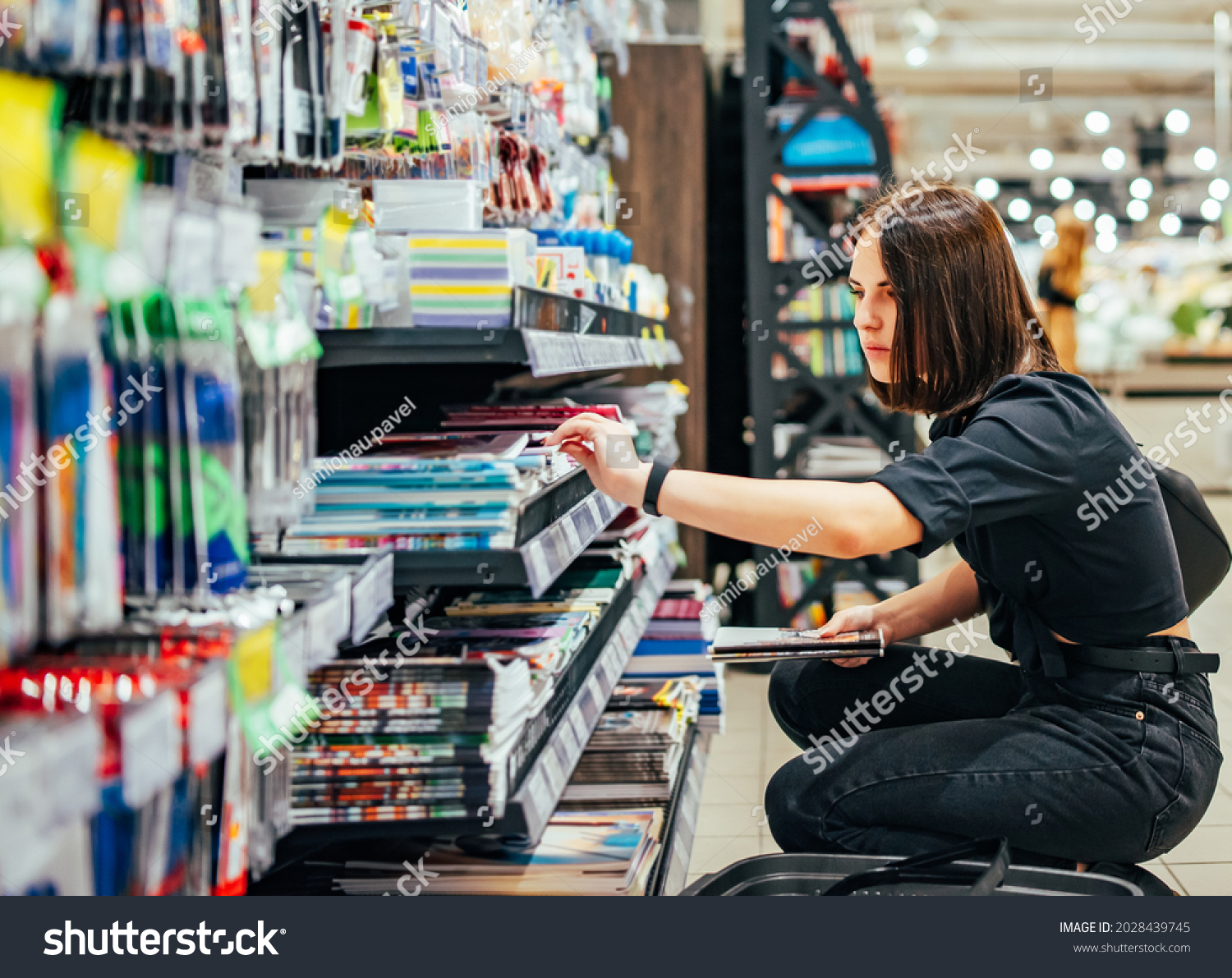 Portrait of young woman choosing school stationery in supermarket. #2028439745