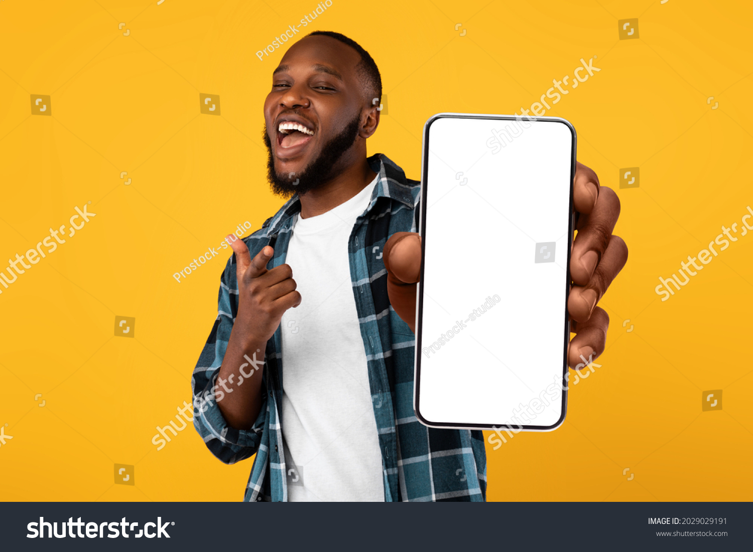 Recommendation. Portrait of excited black guy holding big smartphone with white blank screen in hand, showing close to camera and pointing at device. Gadget with empty free space for mock up, banner #2029029191