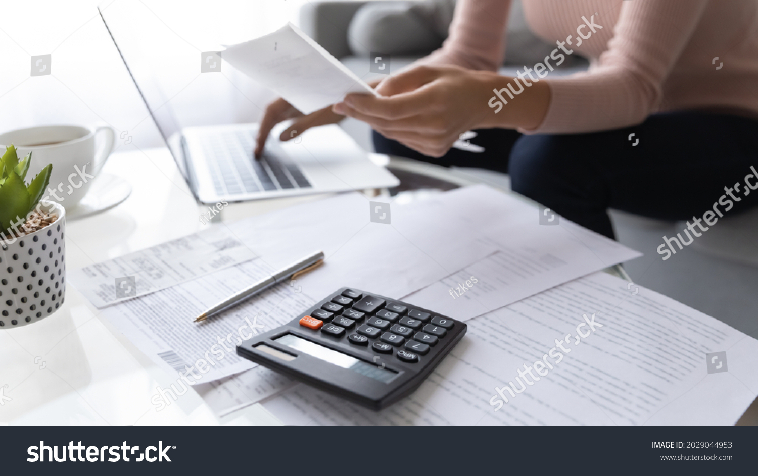 Accountant woman pay bills online use e-bank app, calculating household finances or taxes sit on sofa at home office. Family expenditures management, close up focus on calculator and heap of receipts #2029044953
