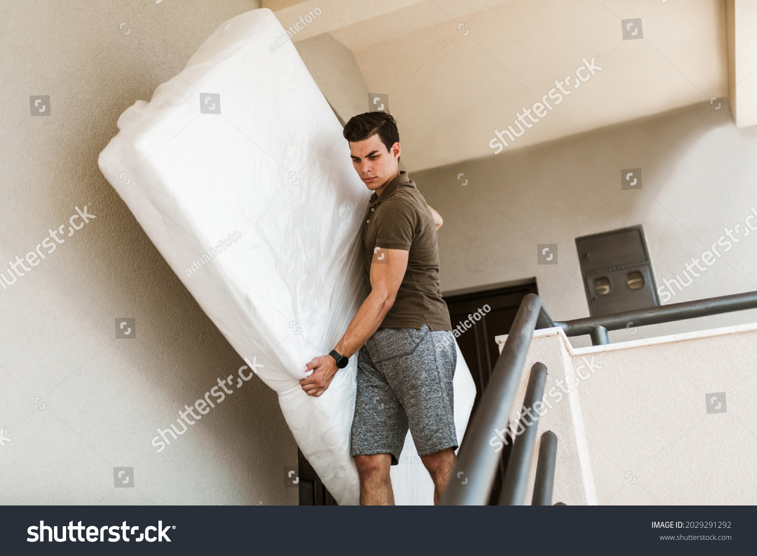 Man carrying the mattress while moving downward the staircase #2029291292