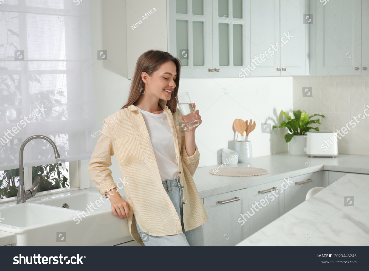 Woman drinking tap water from glass in kitchen #2029443245