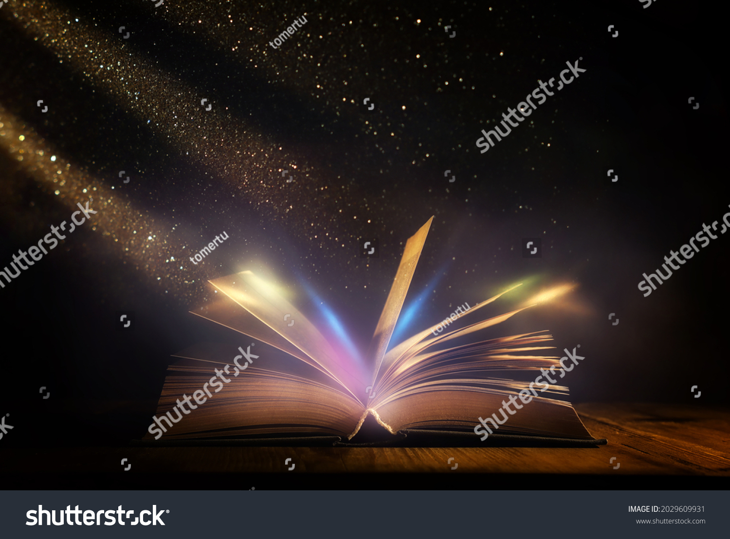 Magical image of open antique book over wooden table with glitter lights #2029609931