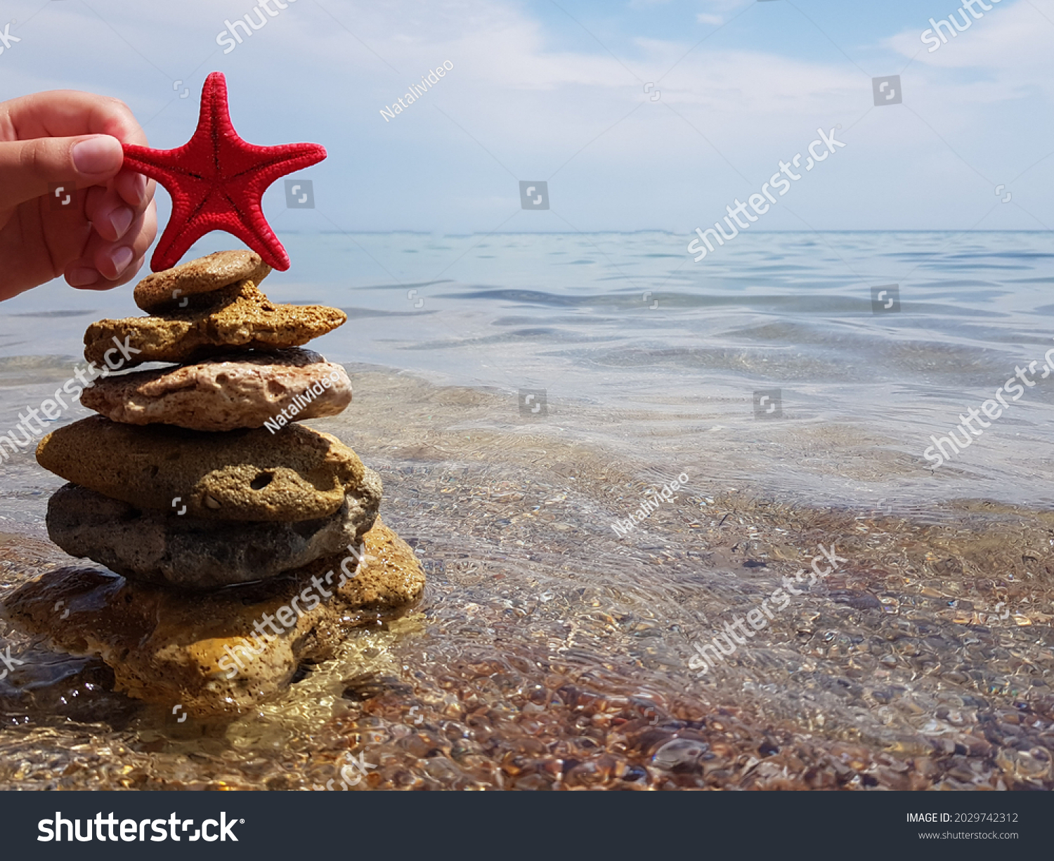 Christmas tree made of sea pebbles on the background of the sea. a red star adorns it. new year on the beach. winter holiday #2029742312