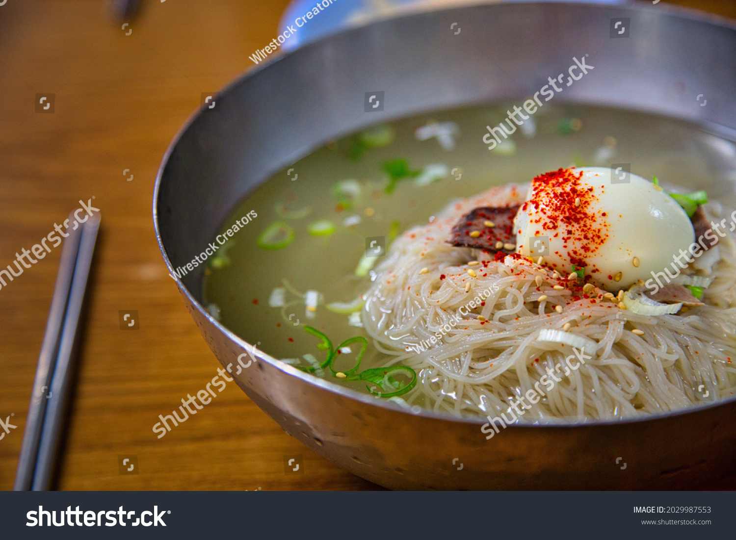 A close-up shot of  plate of pyongyang naengmyeon noodles and chopsticks on teh wooden table #2029987553