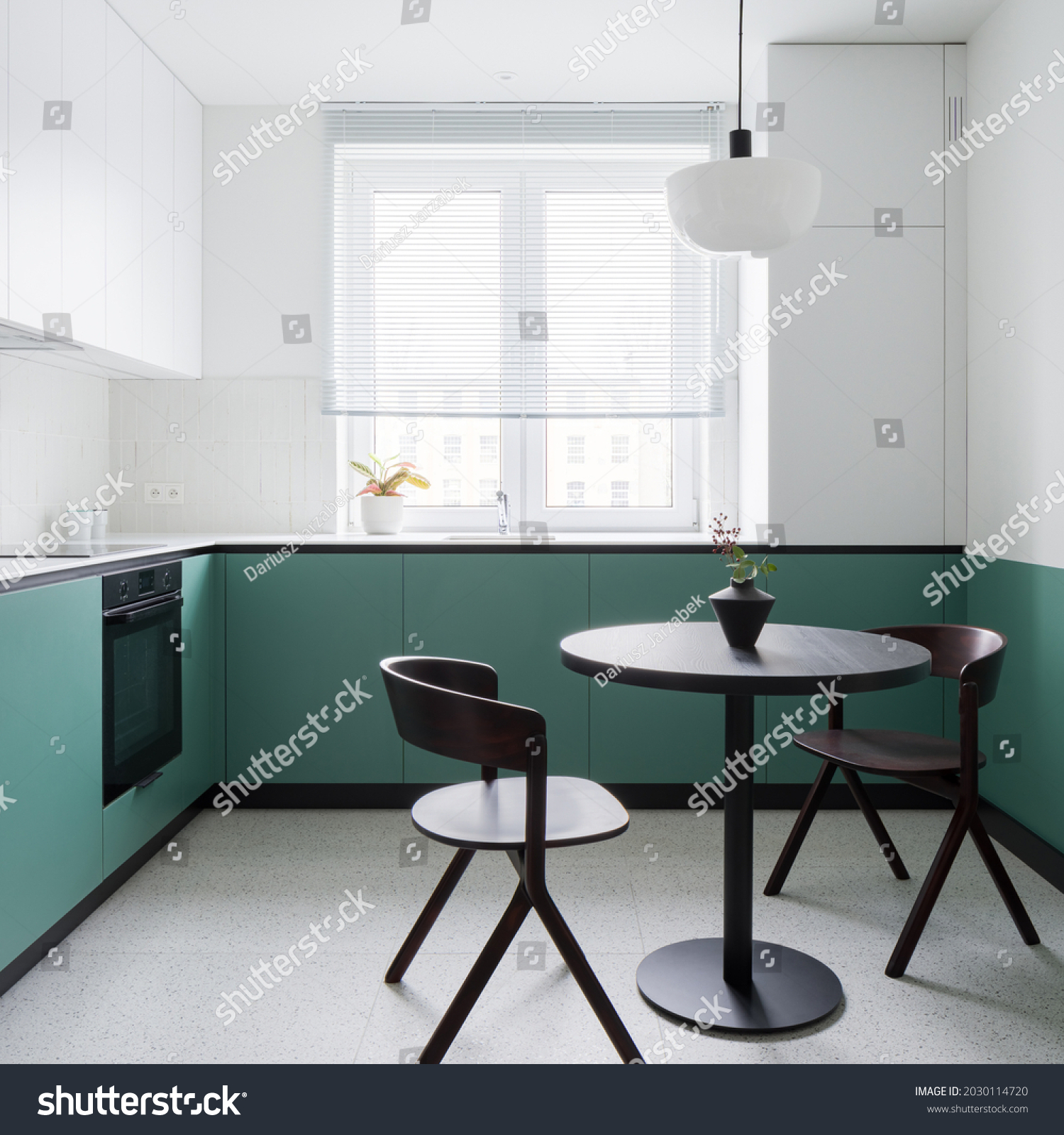 Small and modern kitchen with stylish terrazzo floor, trendy, black dining table with two chairs and stylish white and green walls and cupboards #2030114720