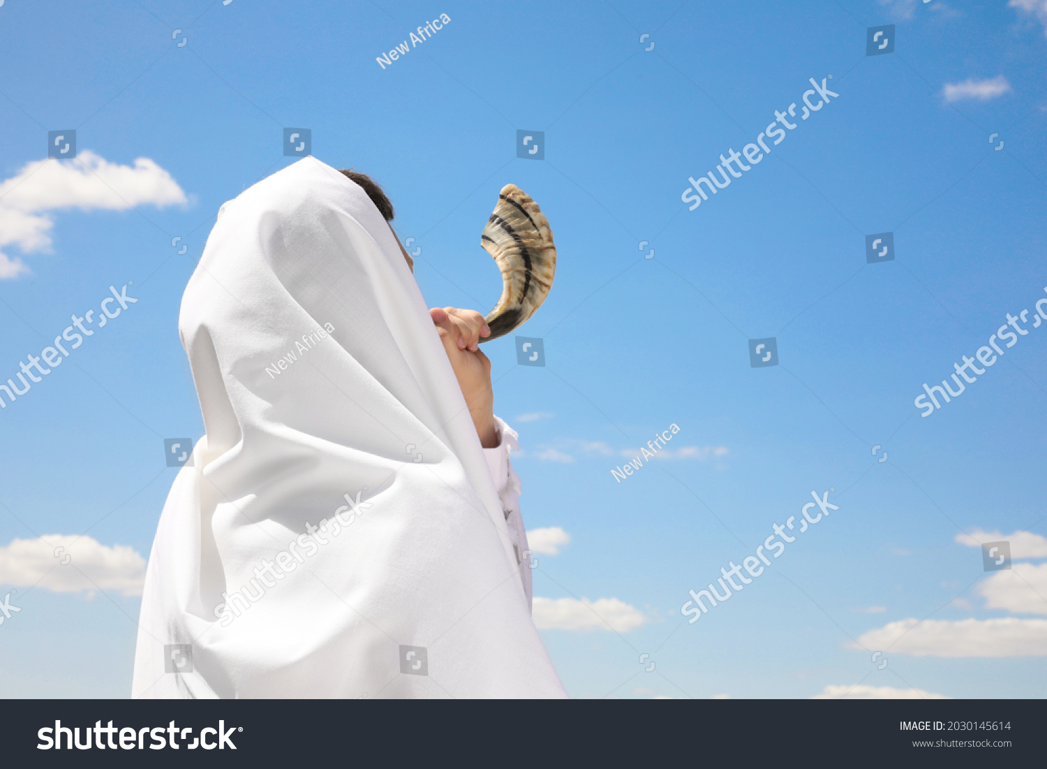 Jewish man in tallit blowing shofar outdoors. Rosh Hashanah celebration #2030145614