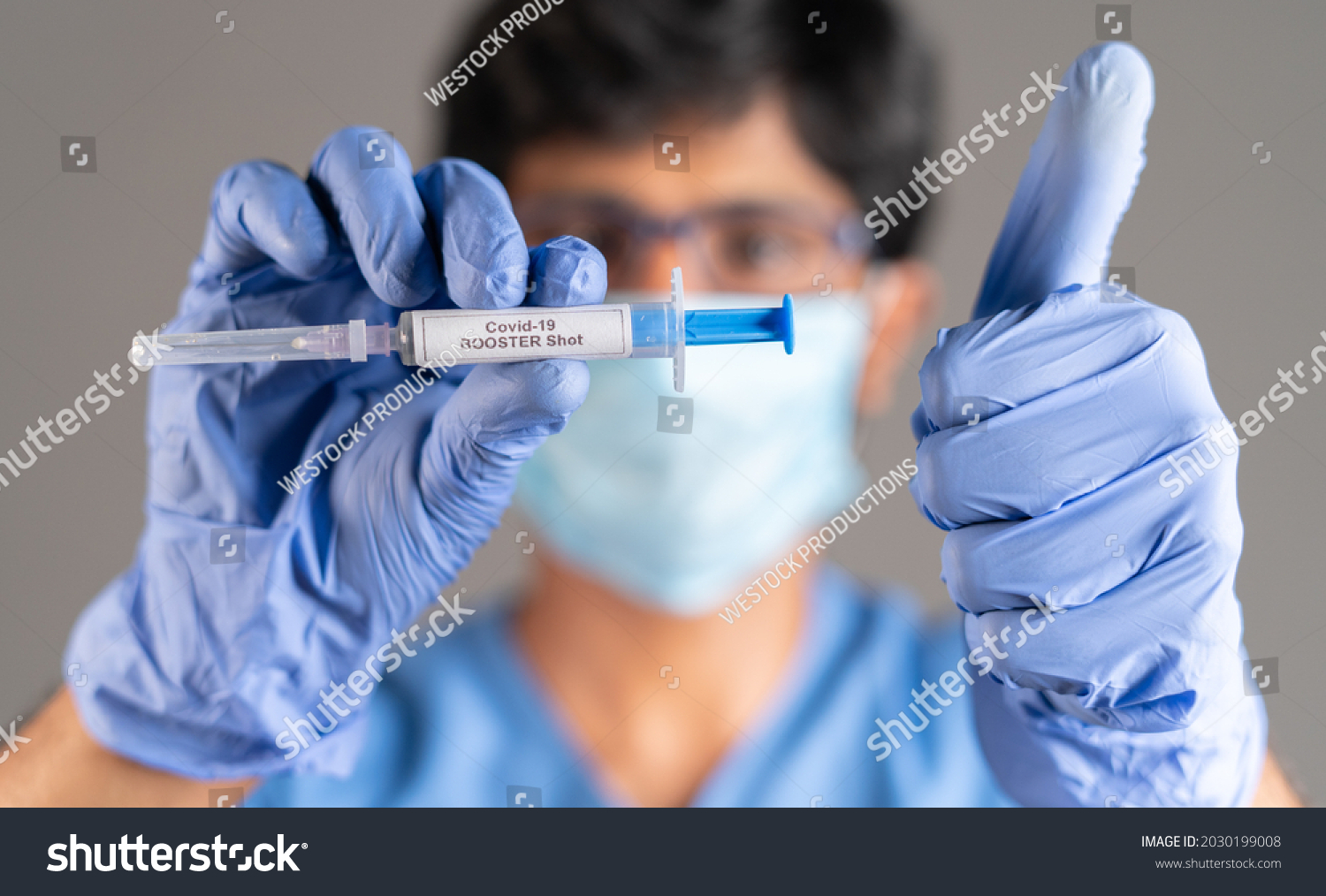 Close up of doctor hands with covid-19 booster shot syringe showing thumbs up - concept showing of recommendation of 3rd dose vaccination for immune weakened people. #2030199008