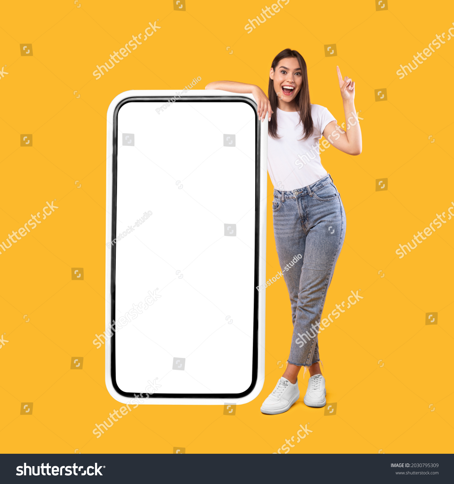 Wow. Happy Woman Leaning On Big Smartphone With Blank White Screen And Pointing Finger Up, Cheerful Lady Recommending New App Or Website, Standing On Yellow Background, Mock Up Image, Full Body Length #2030795309