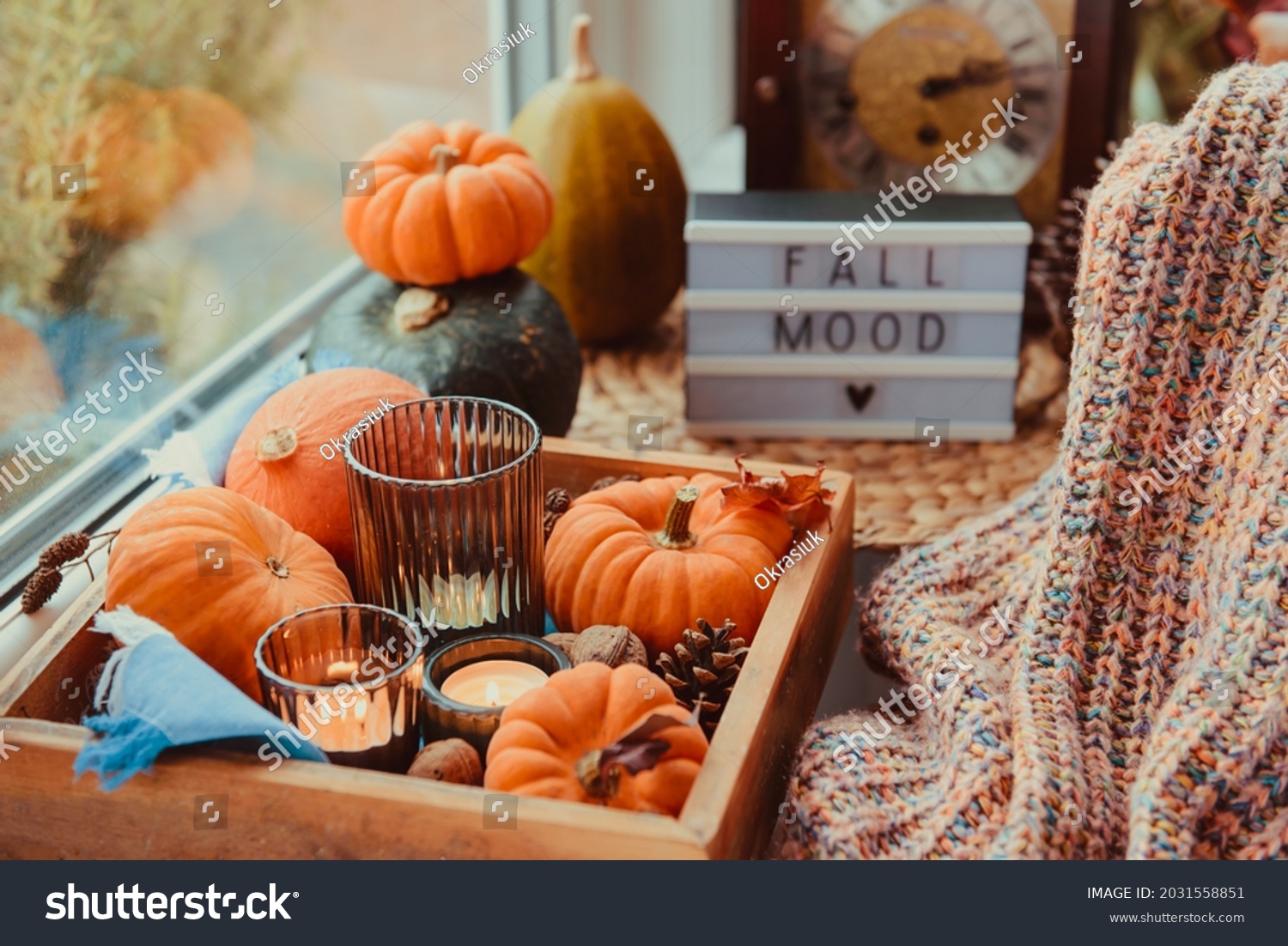 Autumn cozy mood composition on the windowsill. Pumpkins, cones, candles on wooden tray, blurred Fall mood message on lightbox, warm plaid. Autumn, fall, hygge home decor. Selective focus. Copy space. #2031558851
