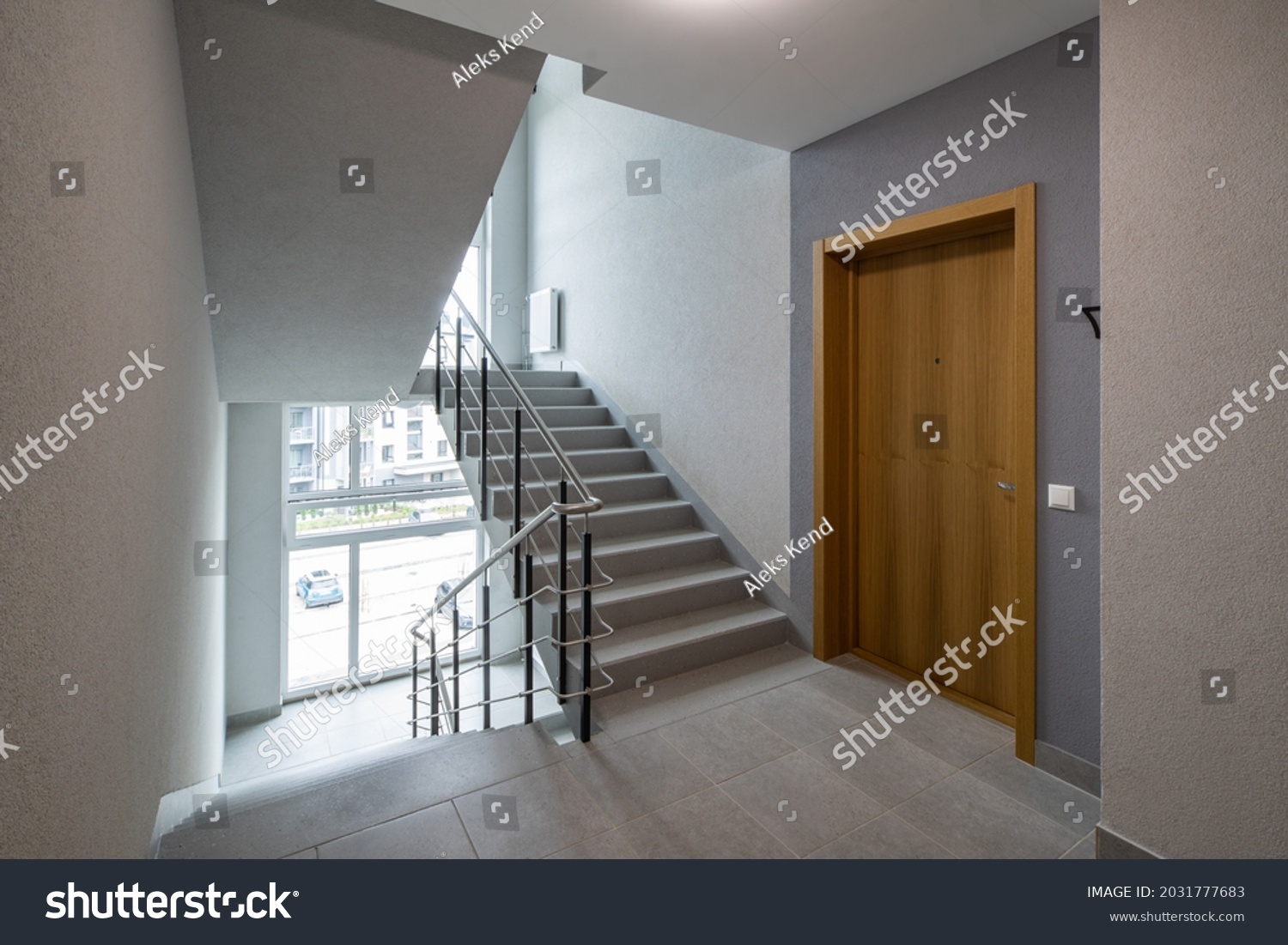 Modern interior of new entrance in residential building. Wooden door to apartment. Stairs and windows. #2031777683
