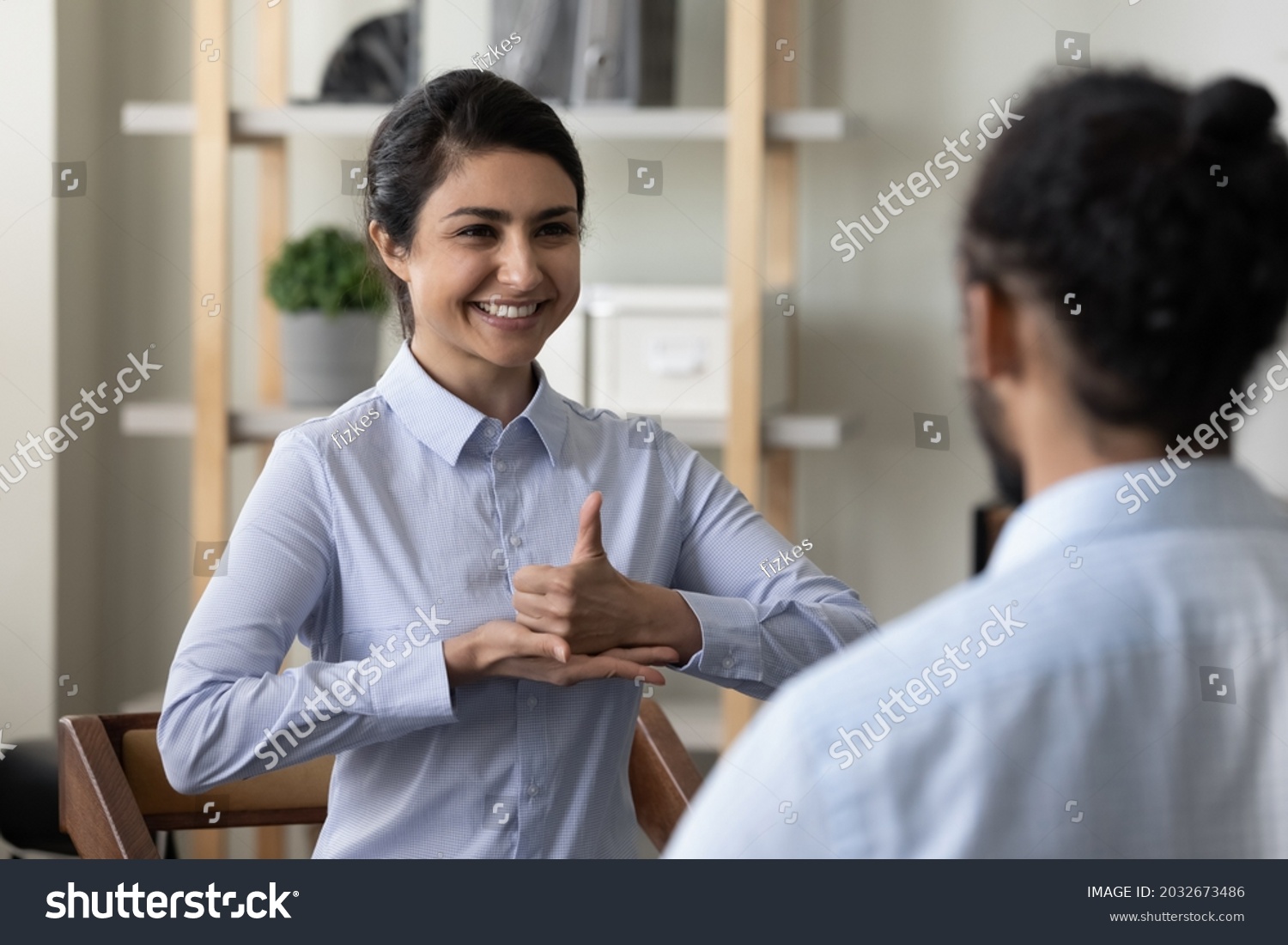 Happy young indian ethnic woman making gestures, practicing sign language with african american friend or therapist, diverse millennial people communicating, enjoying pleasant conversation indoors. #2032673486