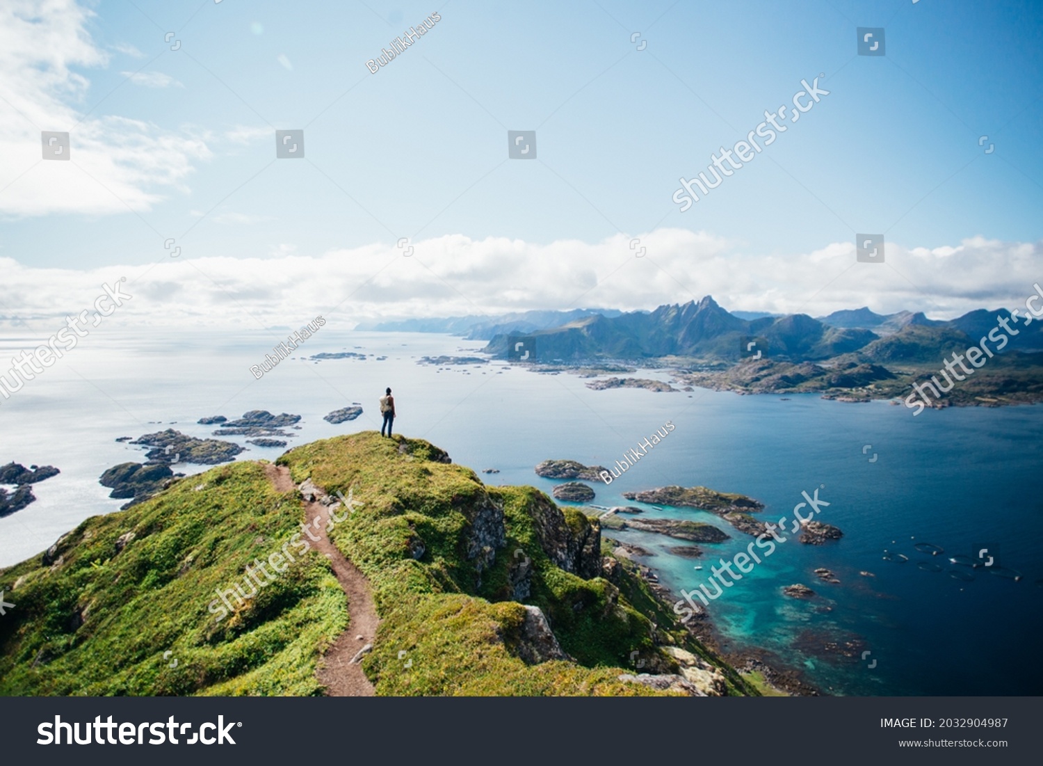 Amazing epic shot of young man hiker stand on top of mountain after long difficult hike in Lofoten Islands in Norway. Incredible summer views of scandinavian travel lifestyle. Epic landscape in north #2032904987