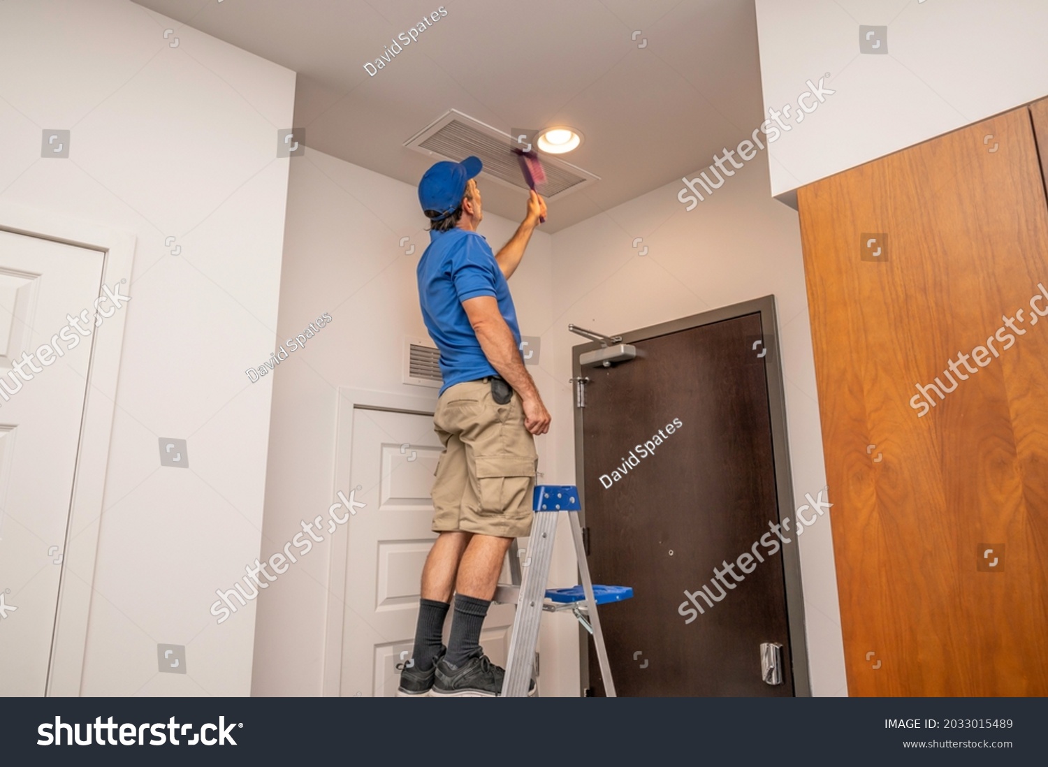 Handyman on a ladder cleaning a return air duct inside of a home #2033015489