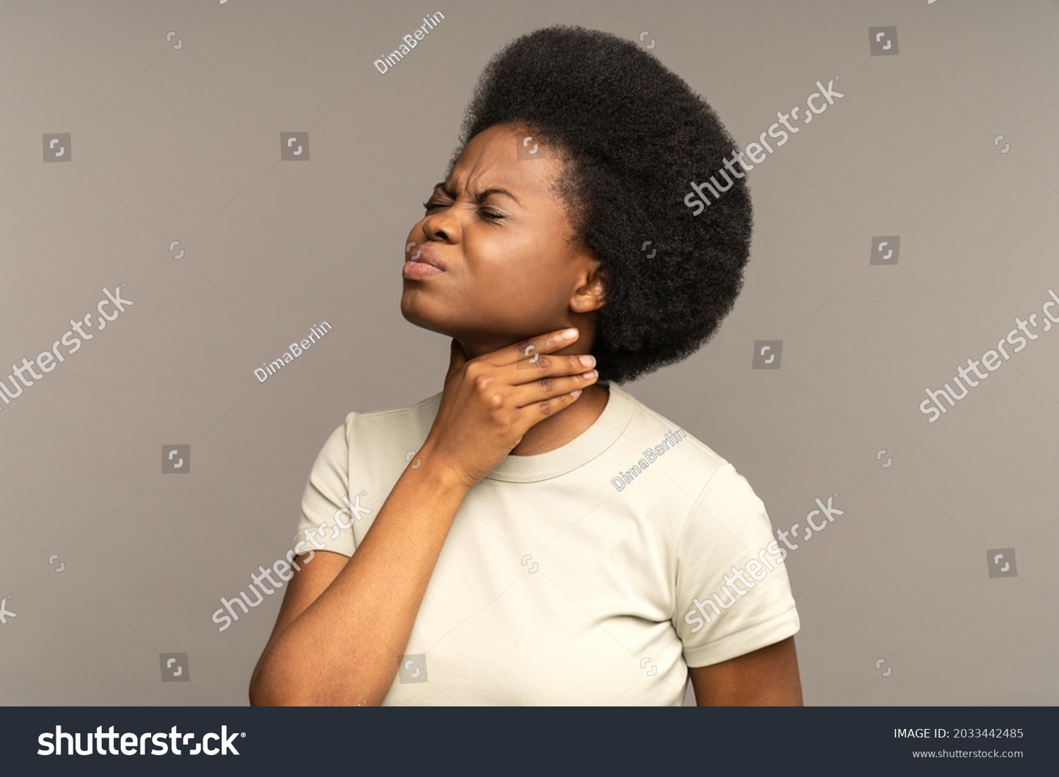 Unhealthy african girl having sore throat, suffering from painful swallowing, strong pain in throat or loss of voice holding neck isolated on studio grey background. Tonsillitis angina thyroid concept #2033442485