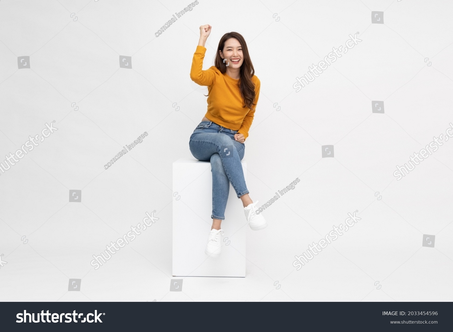 Attractive beautiful Asian woman sitting on white box and hands up raised arms from happiness, Excited female and winner success concept #2033454596