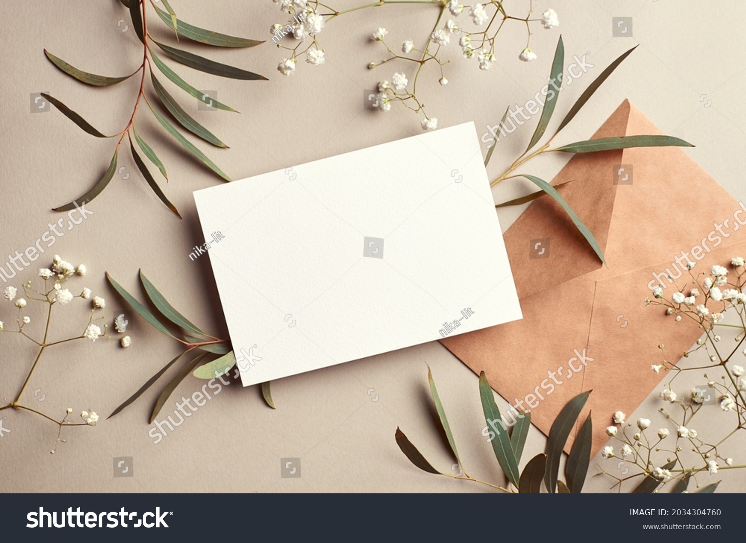 Greeting or invitation card mockup with craft paper envelope, eucalyptus and gypsophila twigs. Card mockup with copy space on beige background. #2034304760