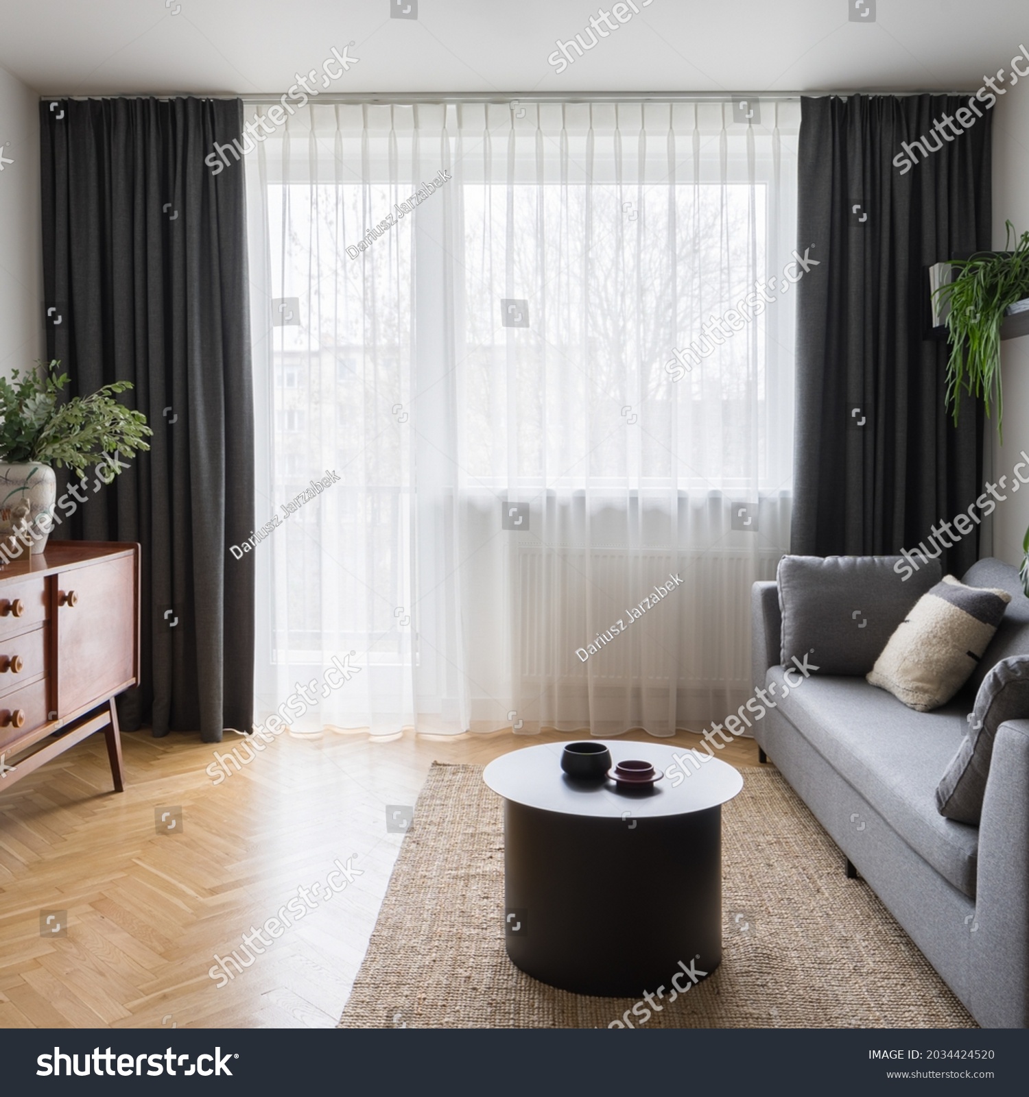 Big window behind decorative curtains in eclectic living room with gray couch, modern coffee table and vintage cupboard #2034424520