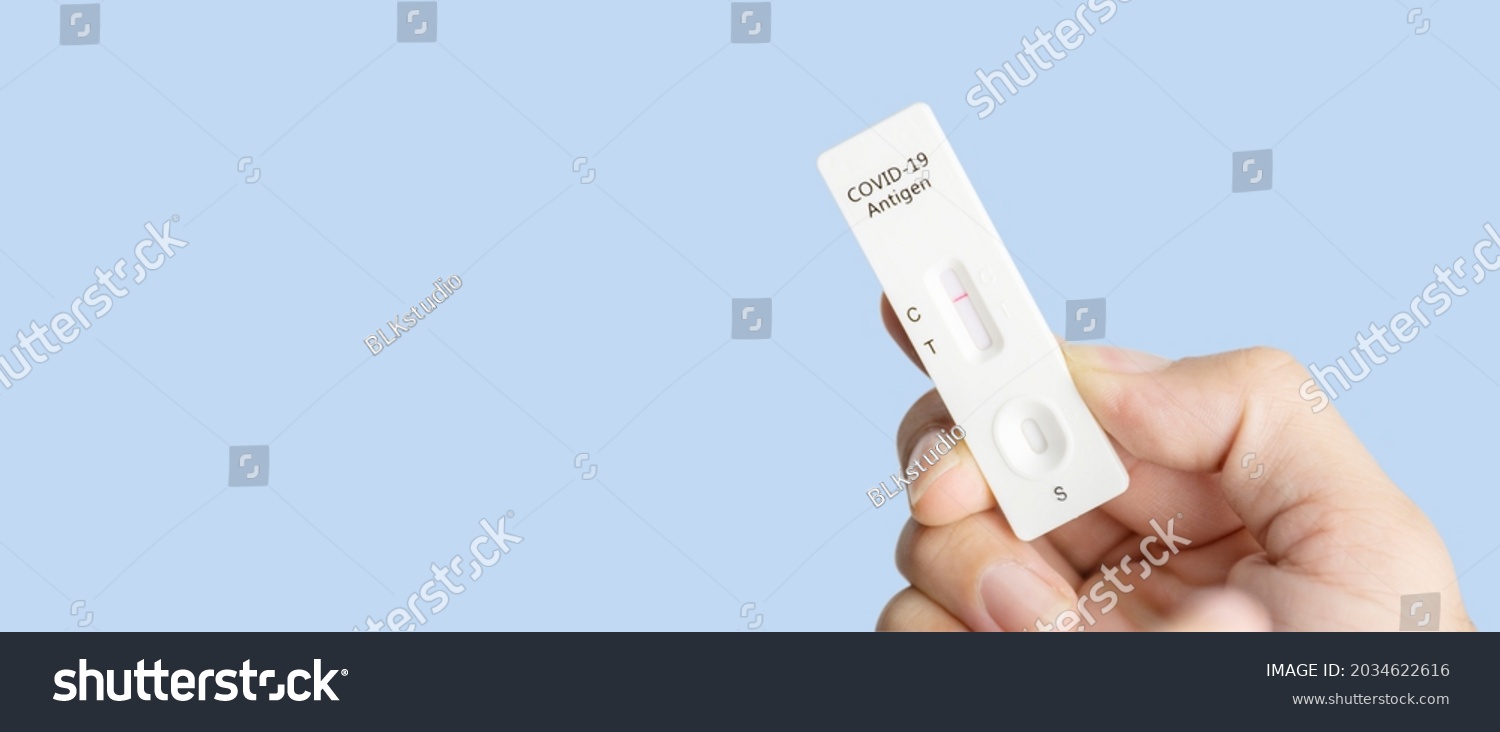 Own hand showing Covid-19 negative test result with SARS CoV-2 Rapid antigen test kit (ATK) and blue background with copy space,Coronavirus infectious protective concept #2034622616