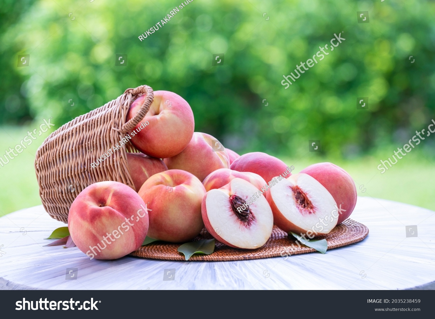 Fresh peach with slices on blurred greenery background, Peach fruit in Bamboo basket on wooden table in garden. #2035238459