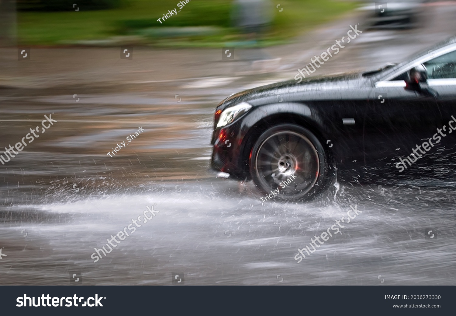 Car driving fast through big puddle at heavy rain, water splashing over the car. Car driving on asphalt road at heavy rain. Dangerous driving conditions. Dangers of aquaplaning. MOTION BLUR #2036273330