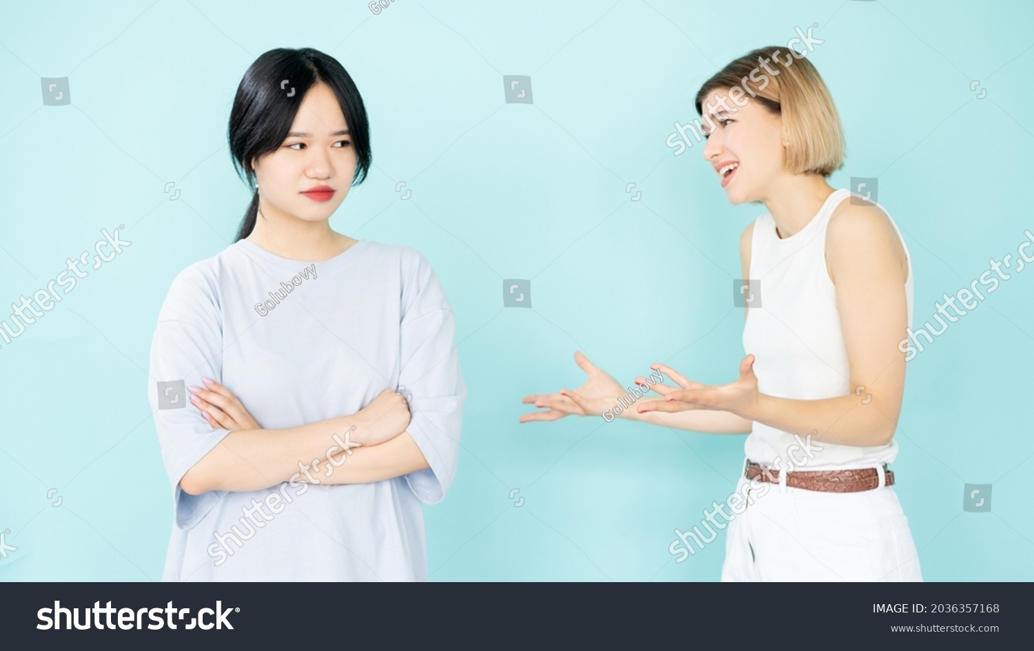 Right proving. Quarrel women. Disagreement arguments. Conflict explanation. Apologizing caucasian lady talking with asian suspicious friend isolated blue. #2036357168