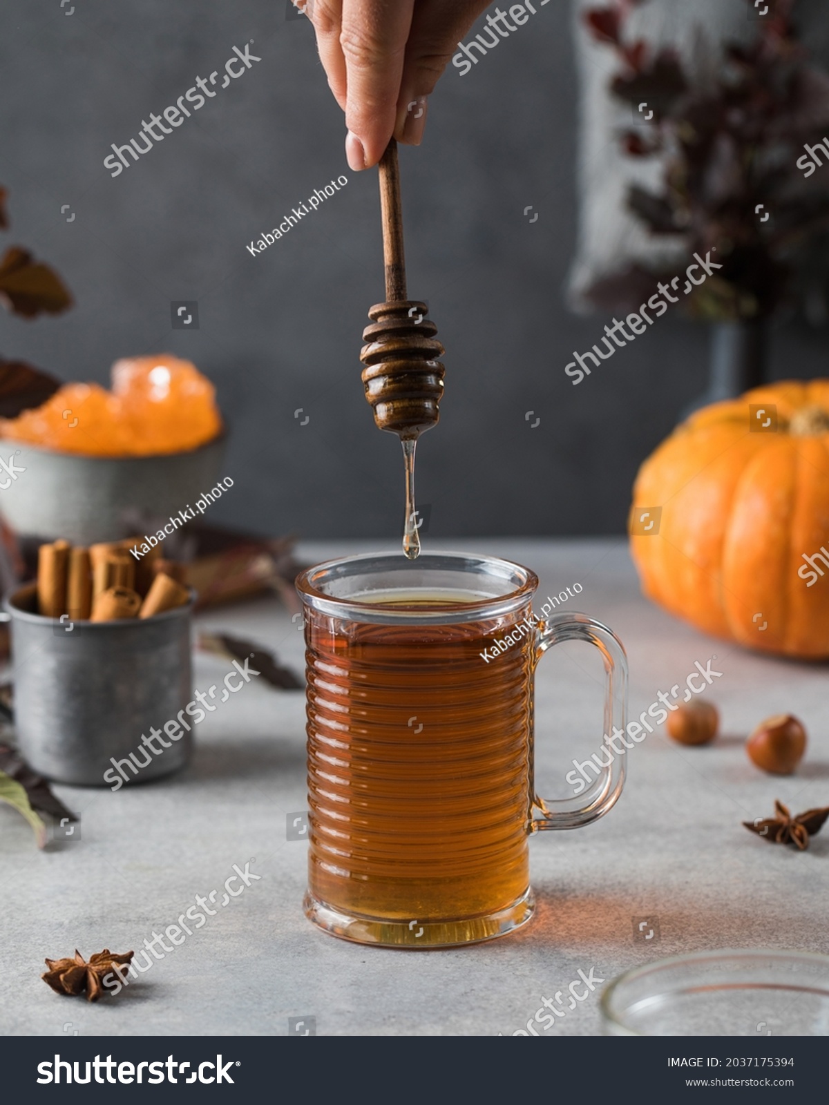 Woman adds honey to fresh hot tea on grey stone table #2037175394