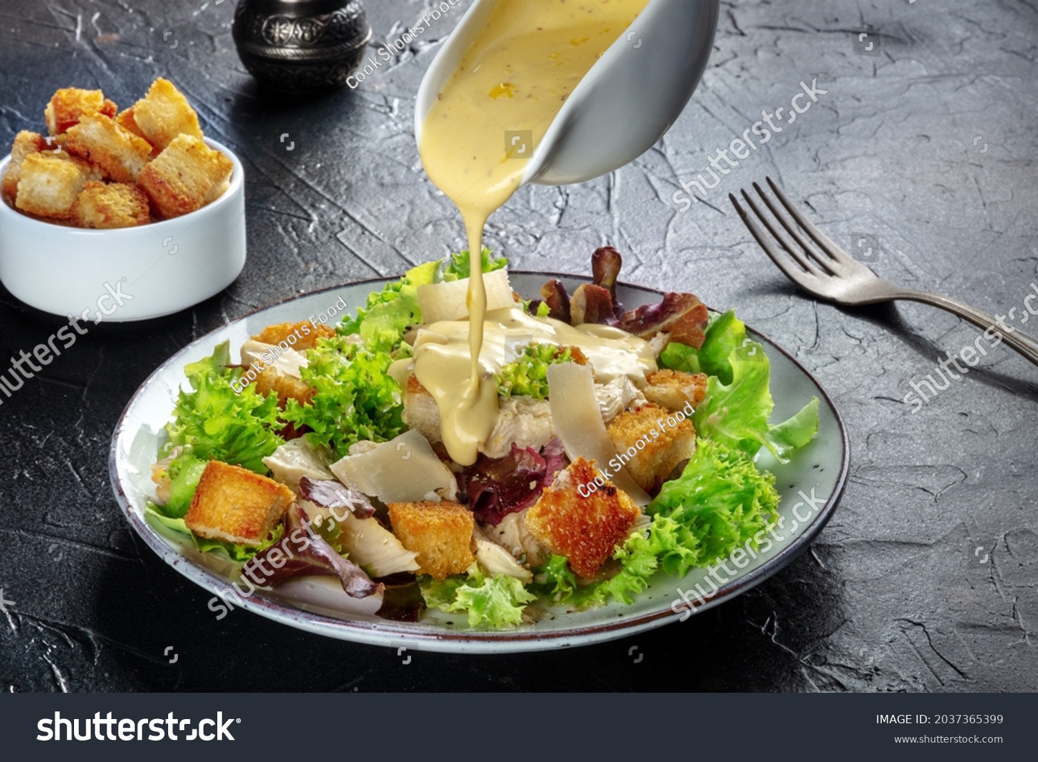 Chicken Caesar salad with the classic dressing being poured, croutons, and pepper, on a black background #2037365399