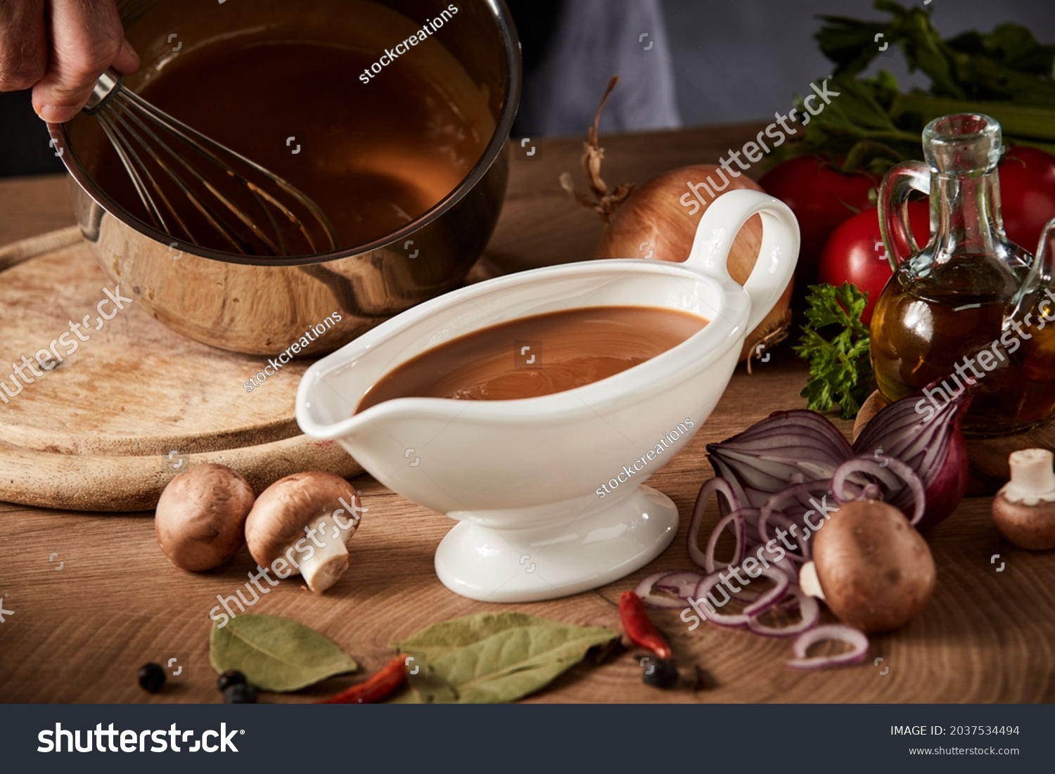 Chef preparing a serving of delicious spicy rich gravy whisking it in a pot with a close up view on a full sauce boat or pitcher in the foreground #2037534494