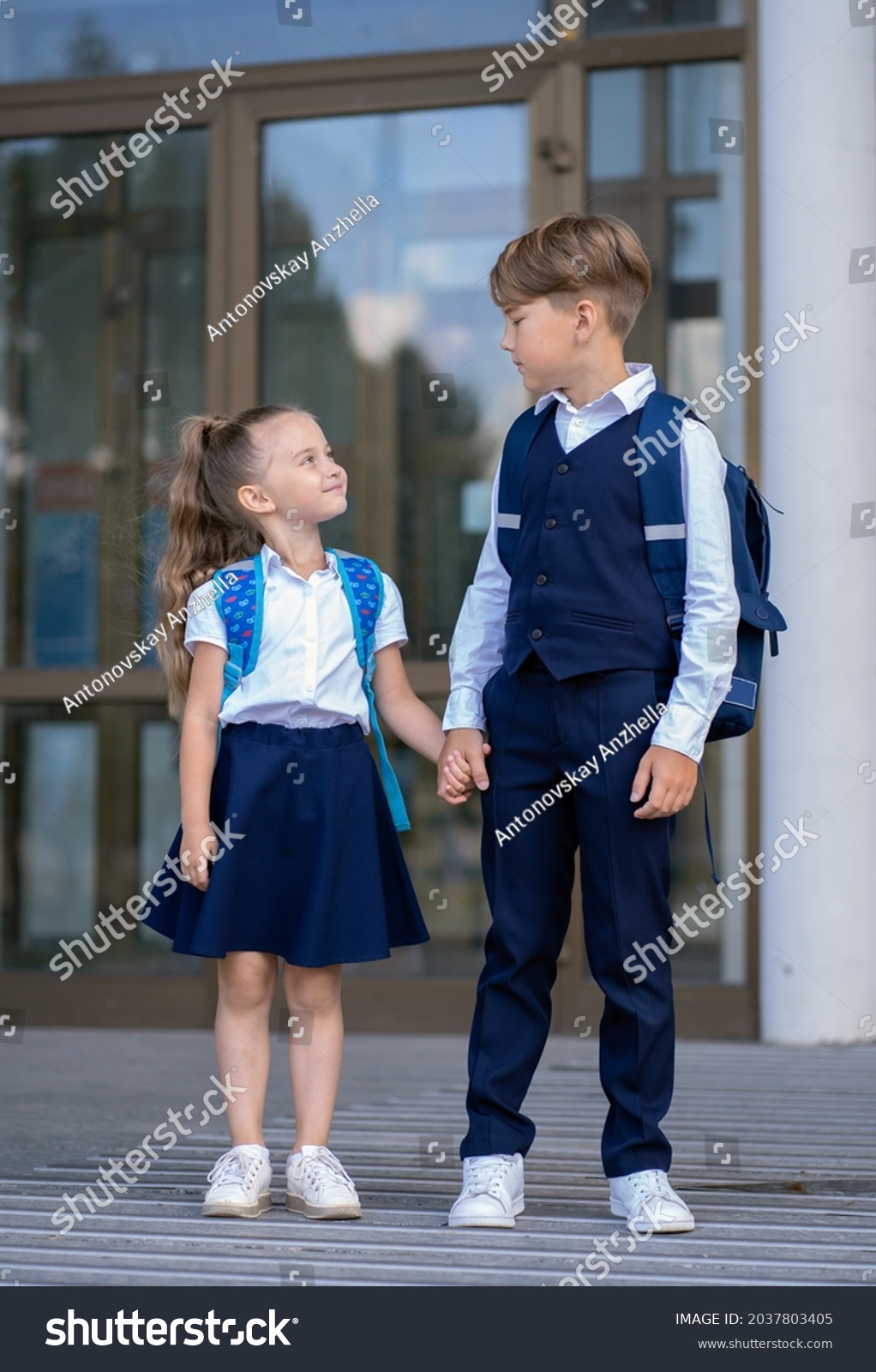 Elder brother and little sister stand in front of the school building holding hands #2037803405