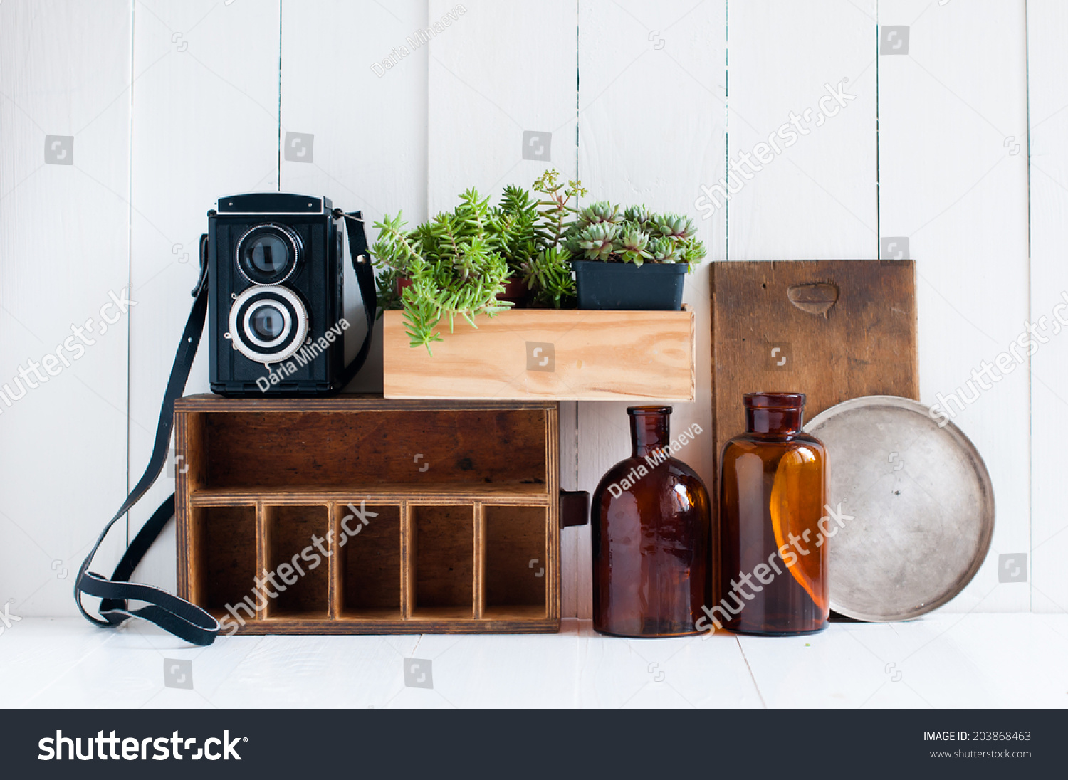 Vintage home decor: old wooden boxes, houseplants, camera and old brown glass bottles on white wooden board, retro home interior. #203868463