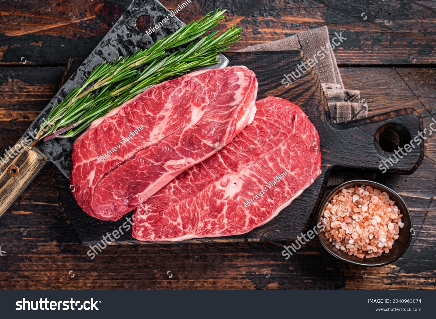 Uncooked Raw Shoulder Top Blade or flat iron beef meat steaks on a wooden butcher board with meat cleaver. Dark wooden background. Top View #2040963074