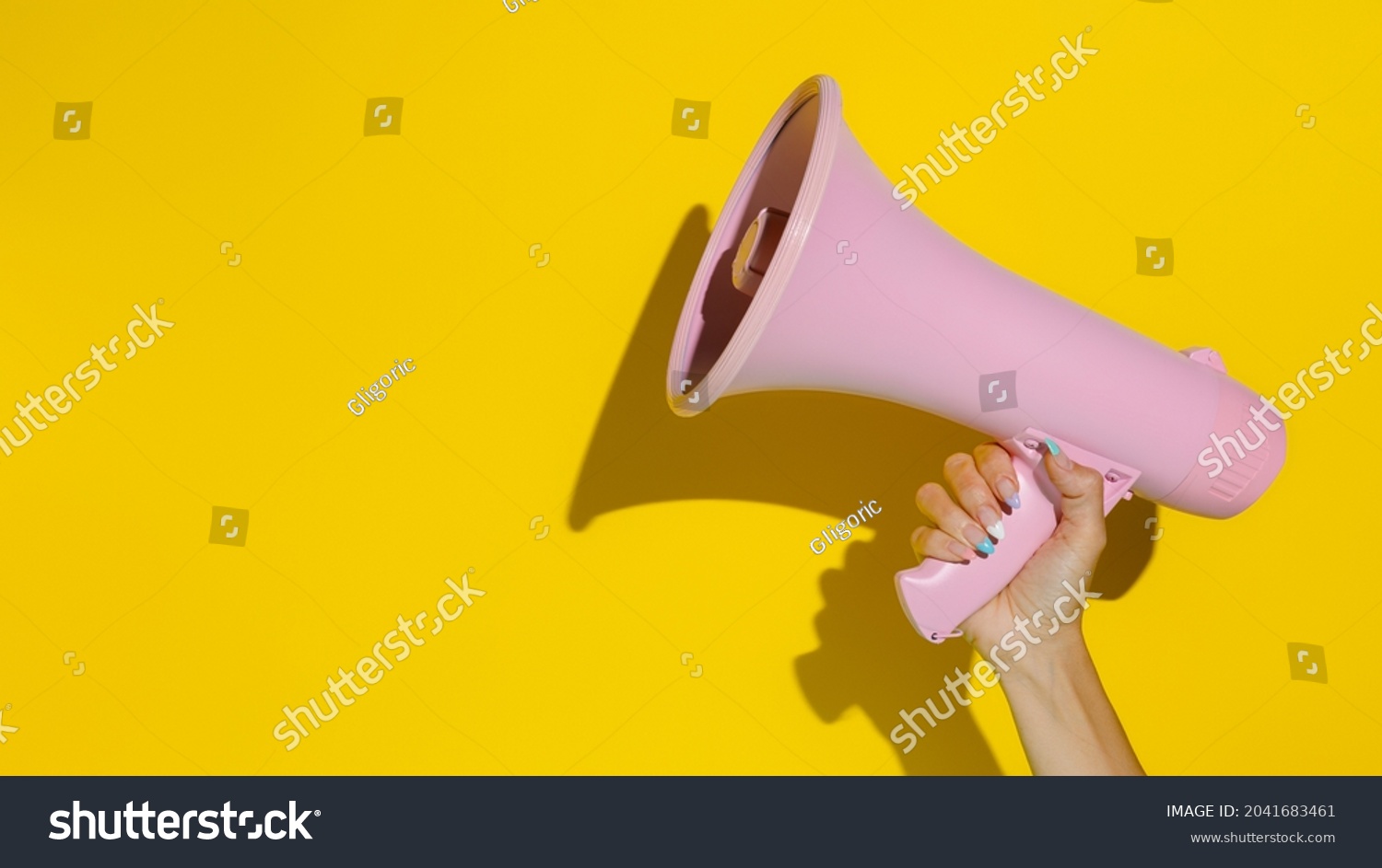A woman's hand holding a pink megaphone isolated on a yellow background. Creative announcement concept. Loud voice of women. Women's rights and voice. Advertisement mock up with copy space for text. #2041683461