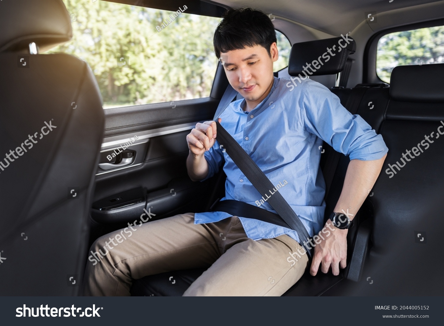 young man fastening a seat belt while sitting in the back seat of car  #2044005152