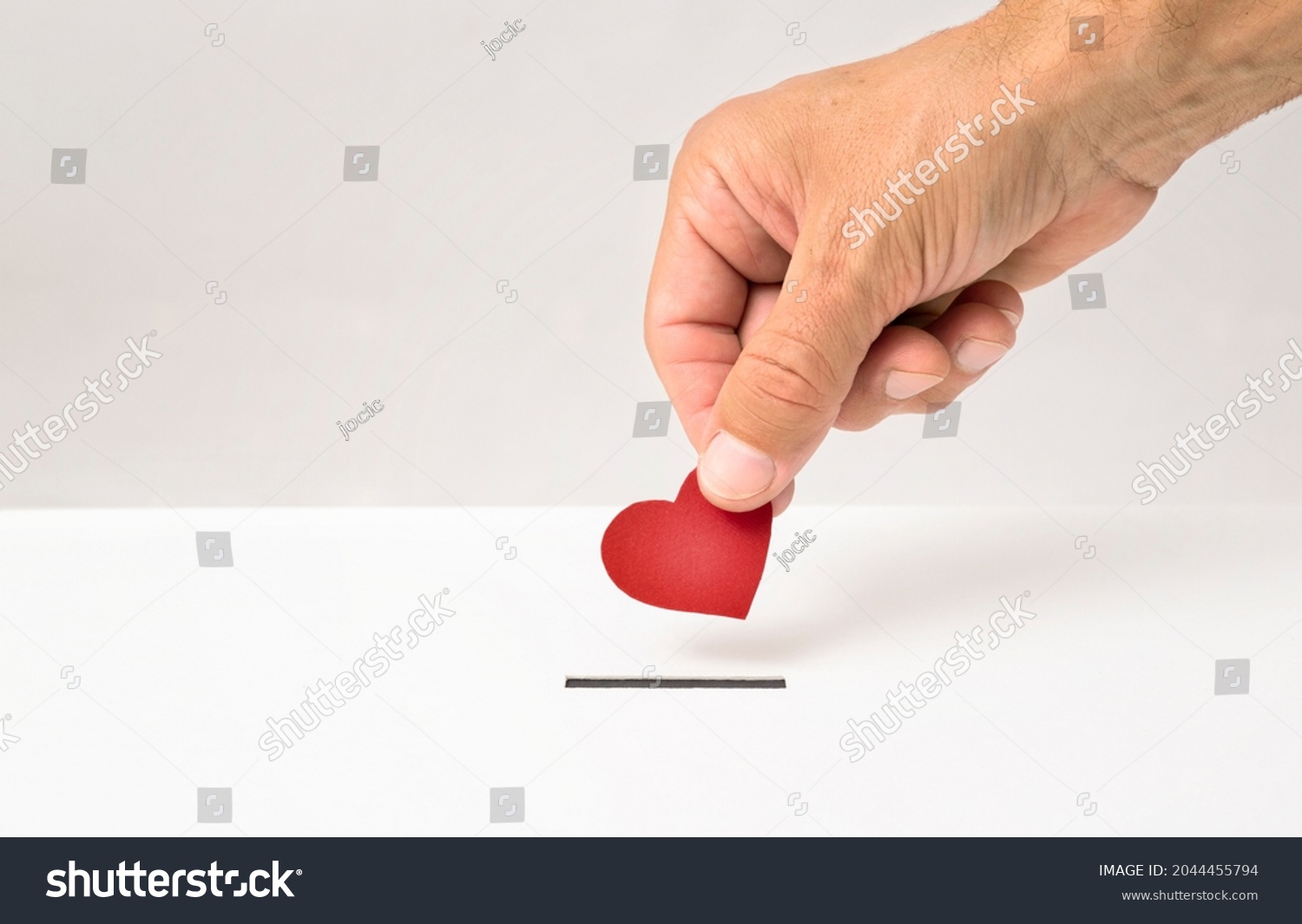 Red heart symbol is put by person's hand into slot of white donation box, Concept of donorship, life saving or charity #2044455794