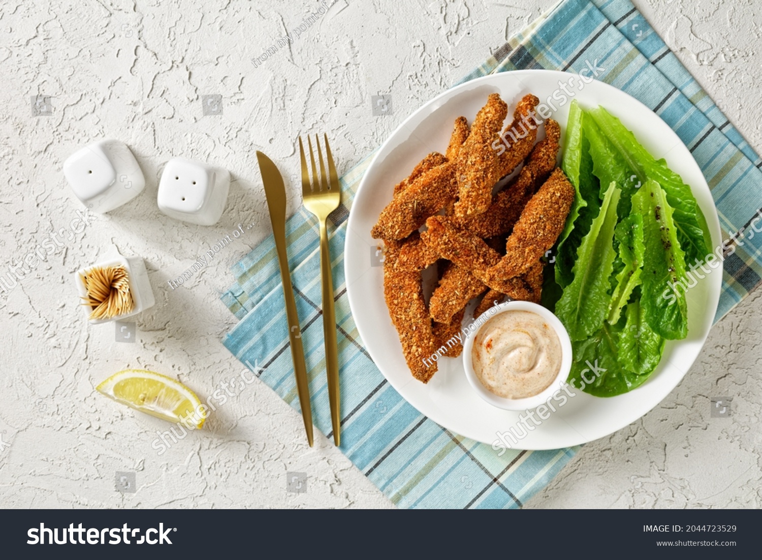 crunchy Baked Chicken Tenders on a white plate with fresh romaine leaves and dipping sauce, horizontal view, american cuisine, flat lay #2044723529