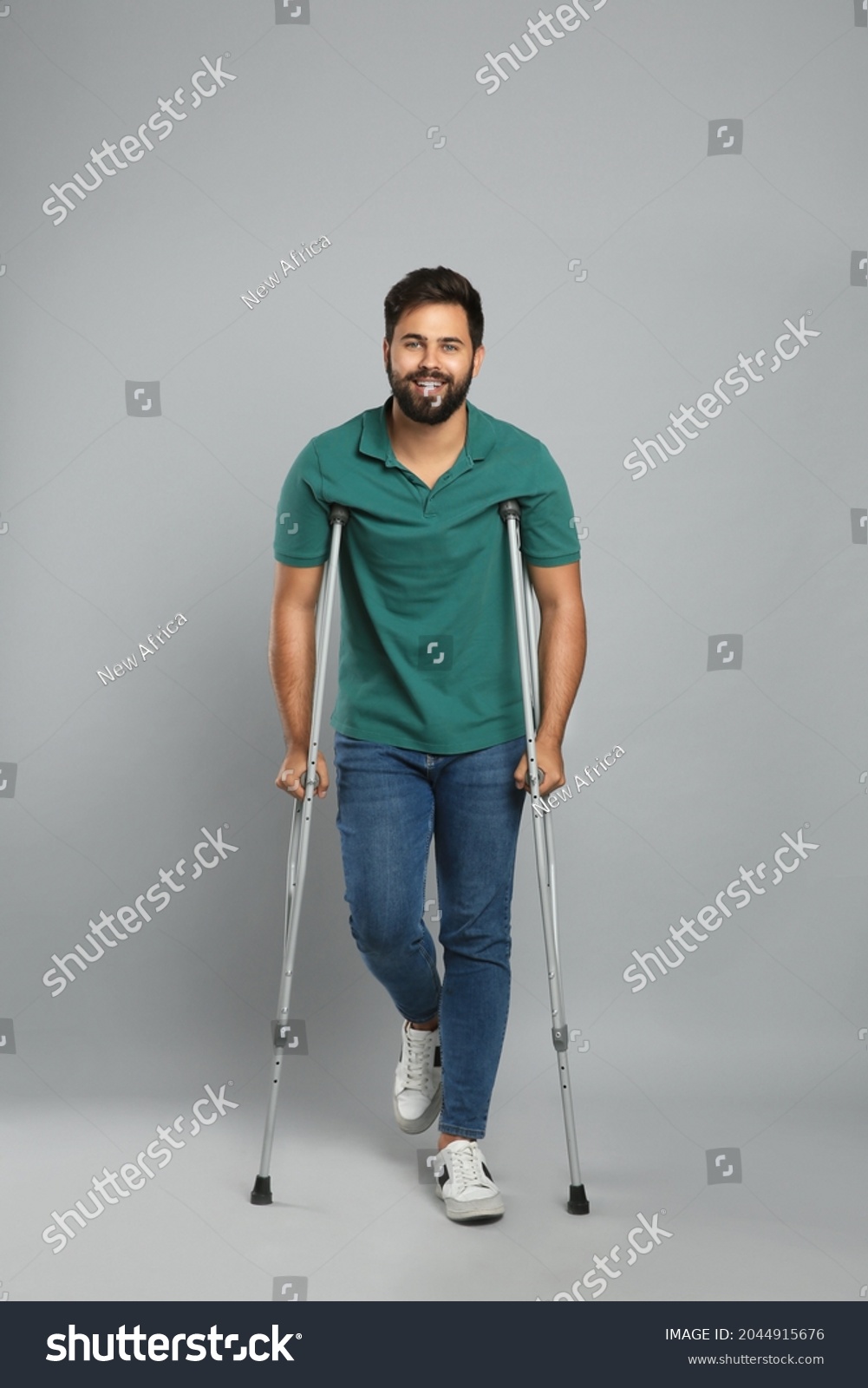 Young man with axillary crutches on grey background #2044915676
