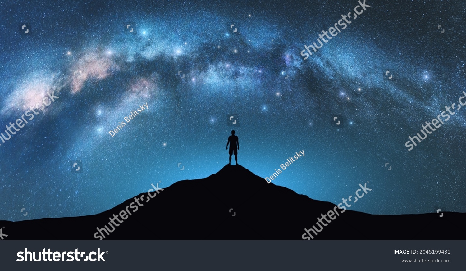 Milky Way arch and man on the mountain peak at starry night. Silhouette of alone guy, blue sky with bright stars in summer. Galaxy. Space background. Landscape with arched milky way. Travel and nature #2045199431