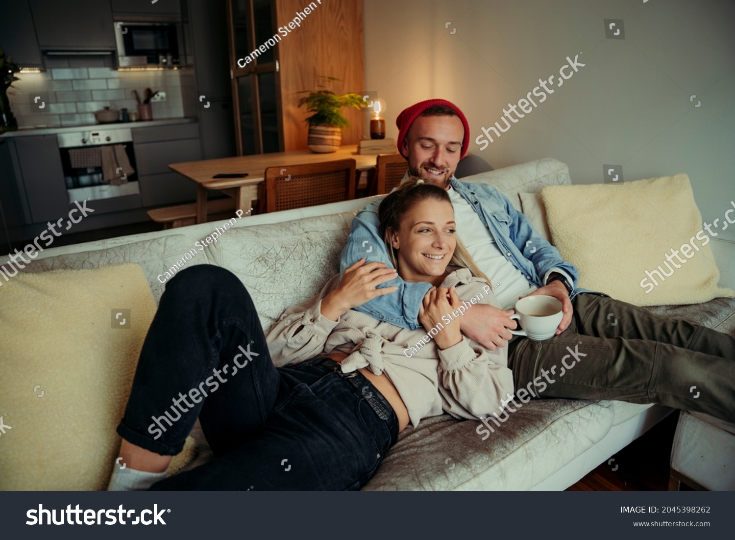 Caucasian couple cuddling on couch hugging each other and smiling  #2045398262