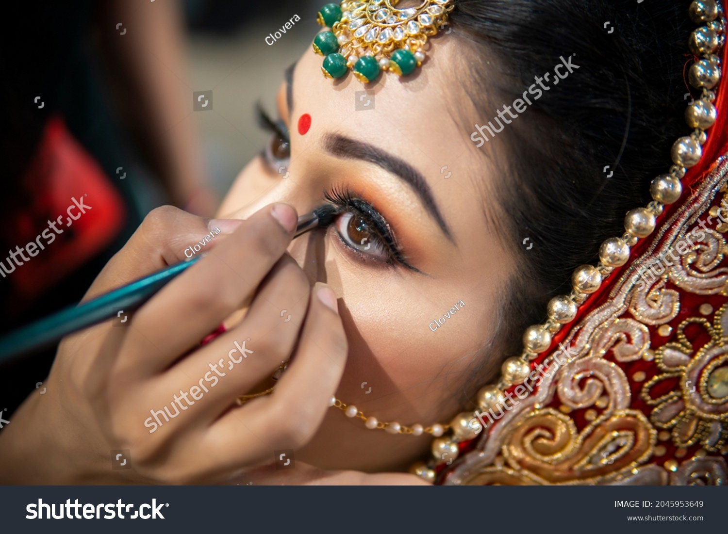 Close up of the beautiful traditional Indian bride getting ready for her wedding day. Cropped hand of makeup artist doing a makeup of bridal face and applying eyeliner. #2045953649
