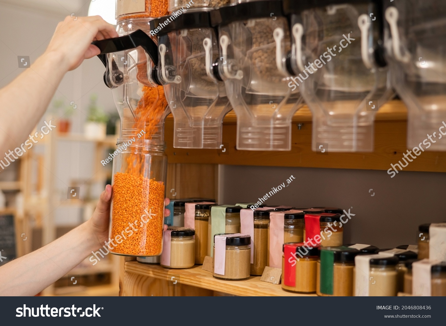 A man fills a jar with red lentils. Selling bulk goods by weight in an eco store. Trade concept without plastic packaging #2046808436