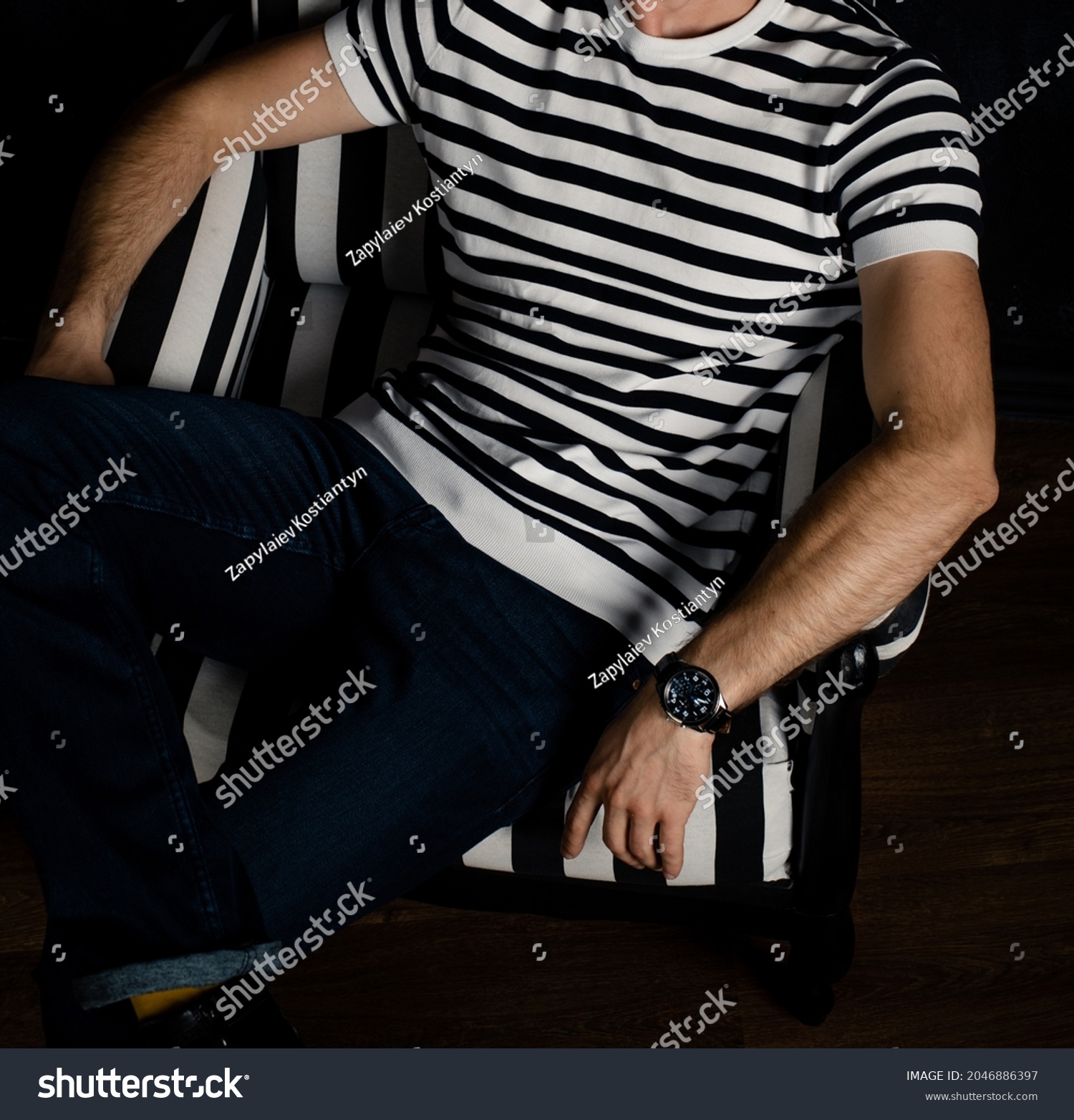 An unrecognizable man in a striped T-shirt sits on a striped armchair. #2046886397