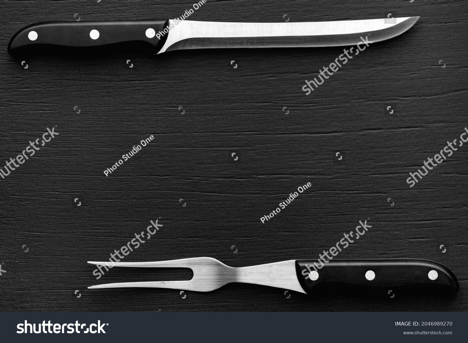 Chef’s carving set. Knife and fork on a black wood with a slightly pronounced texture. Top view with copy space. #2046989270