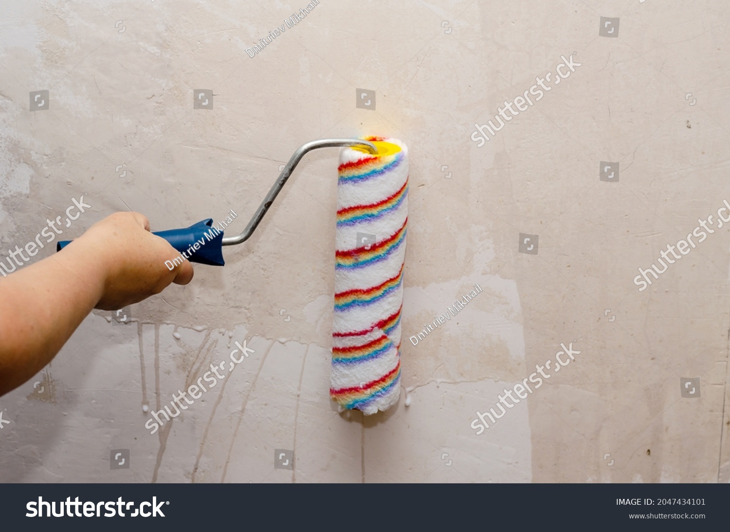 A woman holds a paint roller and impregnates the walls of the room with a primer. Preparing the walls for painting. Inside the room. Selective Focus. #2047434101