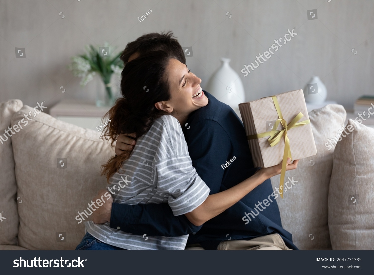 Happy young 30s latina woman embracing loving husband, feeling thankful for getting present in wrapped gift box, celebrating happy birthday or marriage anniversary, international women s day. #2047731335